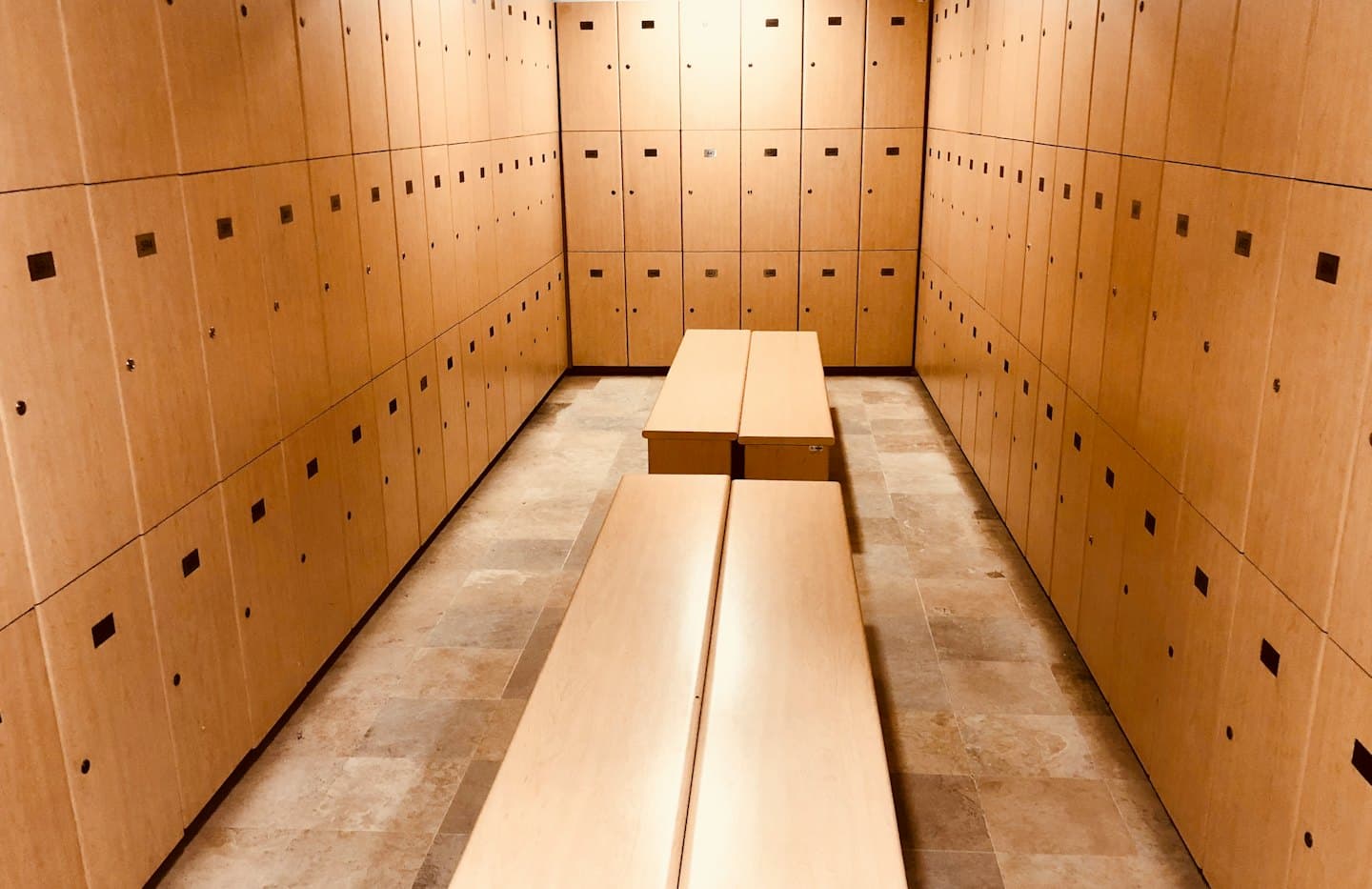 Empty locker room with wooden benches and symmetrical storage lockers.