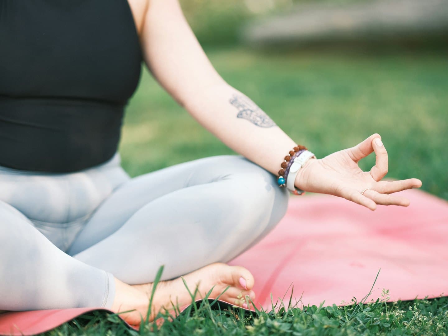 Person meditating outdoors on a red yoga mat with hands in mudra.